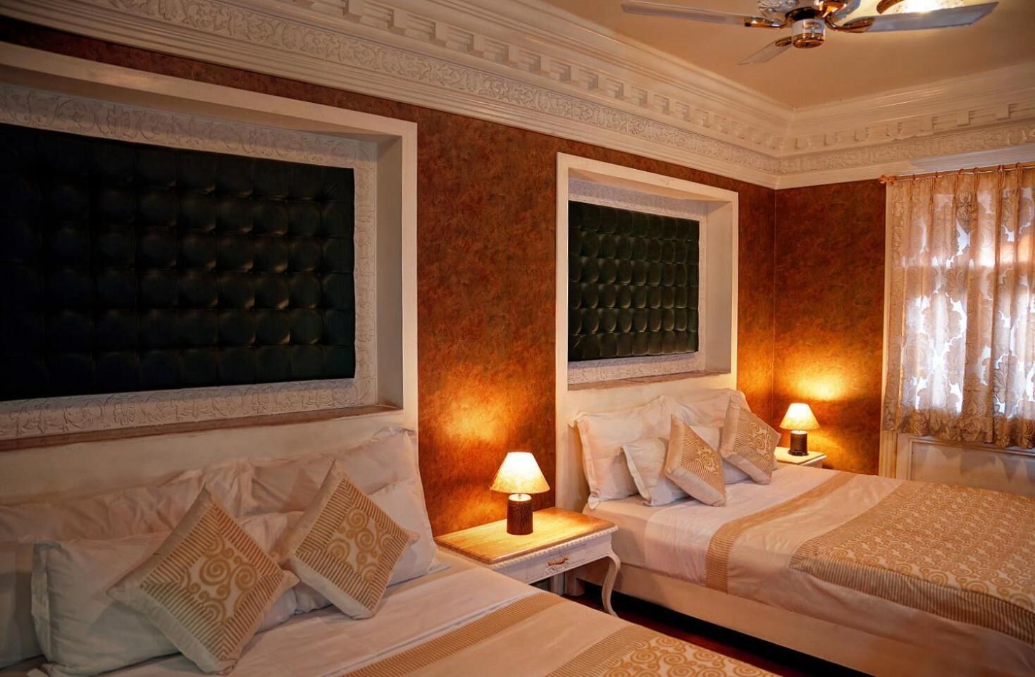 Una camera d'albergo con due letti, ognuno dotato di testiera, un comodino con lampada e una finestra con tende.
