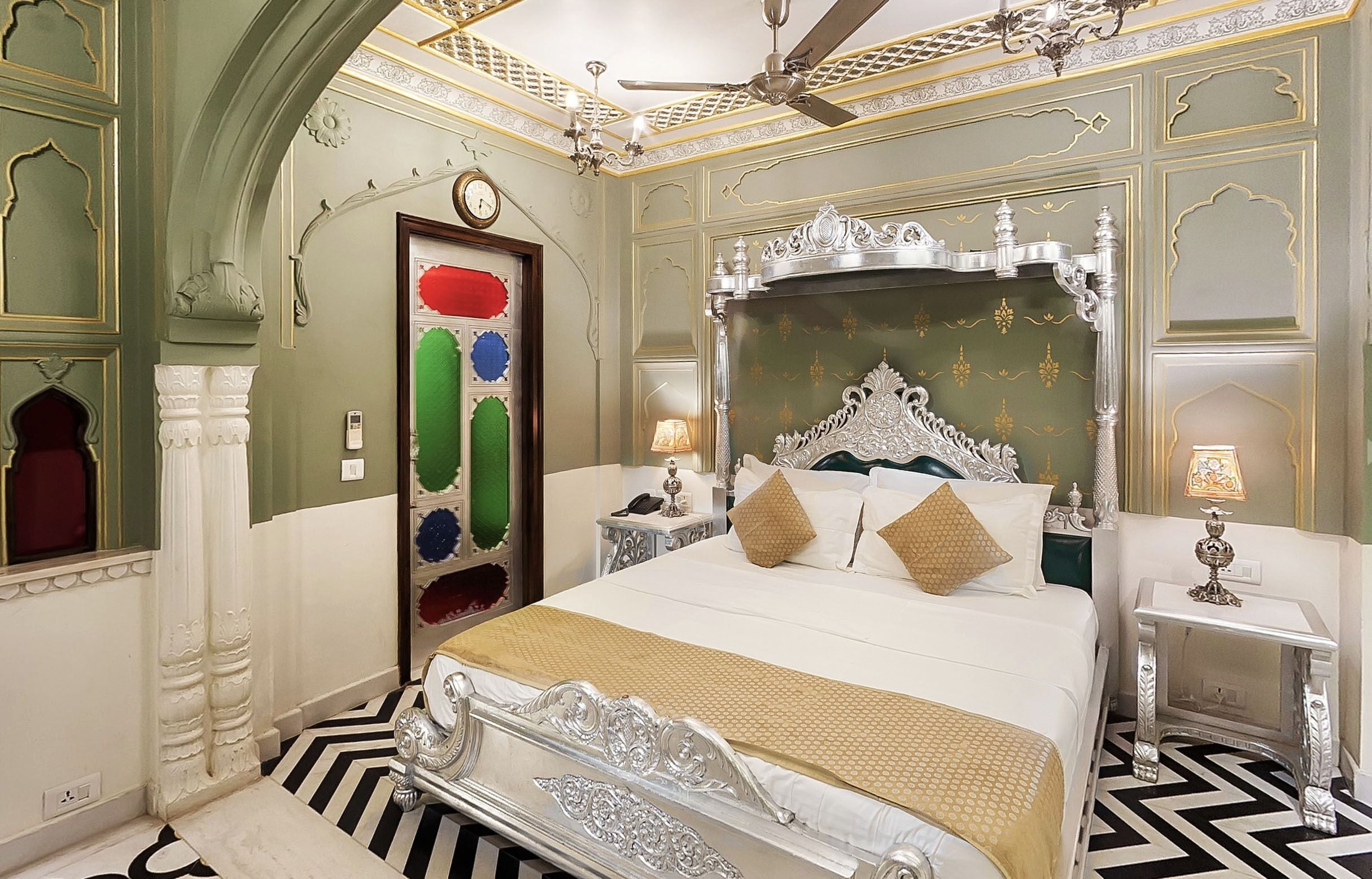 Une chambre à coucher luxueuse, dotée d’un grand lit à baldaquin richement décoré, d’un lustre et d’un miroir décoratif.