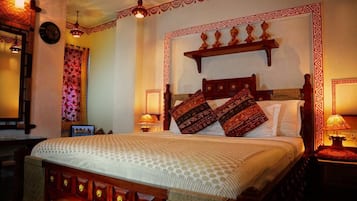Quarto tradicional com cama grande, cabeceira de madeira, almofadas estampadas e painéis decorativos na parede.
