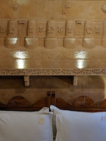 A room with a carved stone wall, a wooden headboard, and two white pillows with embroidered designs.