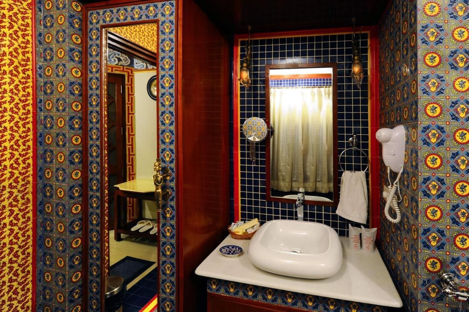 Un bagno con un lavandino bianco, uno specchio e un asciugacapelli. Le pareti sono decorate con piastrelle a motivi.