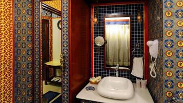 Casa de banho com lavatório branco, espelho e secador de cabelo. As paredes são decoradas com azulejos estampados.