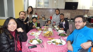 A group of people seated around a table with various dishes, in a room with cabinets and a television. - Shine Nepal Homestay (Kathmandu)