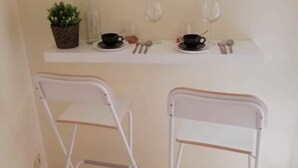A small kitchenette with two white metal chairs, a white countertop, a potted plant, and two wine glasses. - Vetrina Suites (Rome)
