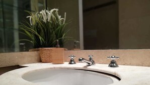 A bathroom sink with a mirror above it, a potted plant, and a wooden basket. - Vetrina Suites (Rome)