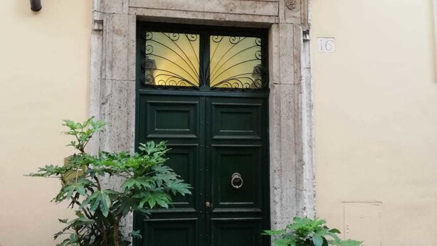 A double door with a decorative architrave and a plaque above it. There are two potted plants on either side of the door. - Vetrina Suites (Rome)