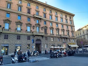 A multi-story building with a classic architectural style, featuring a central entrance, multiple balconies, and a variety of shops on the ground floor. - amoRaRoma (Rome)