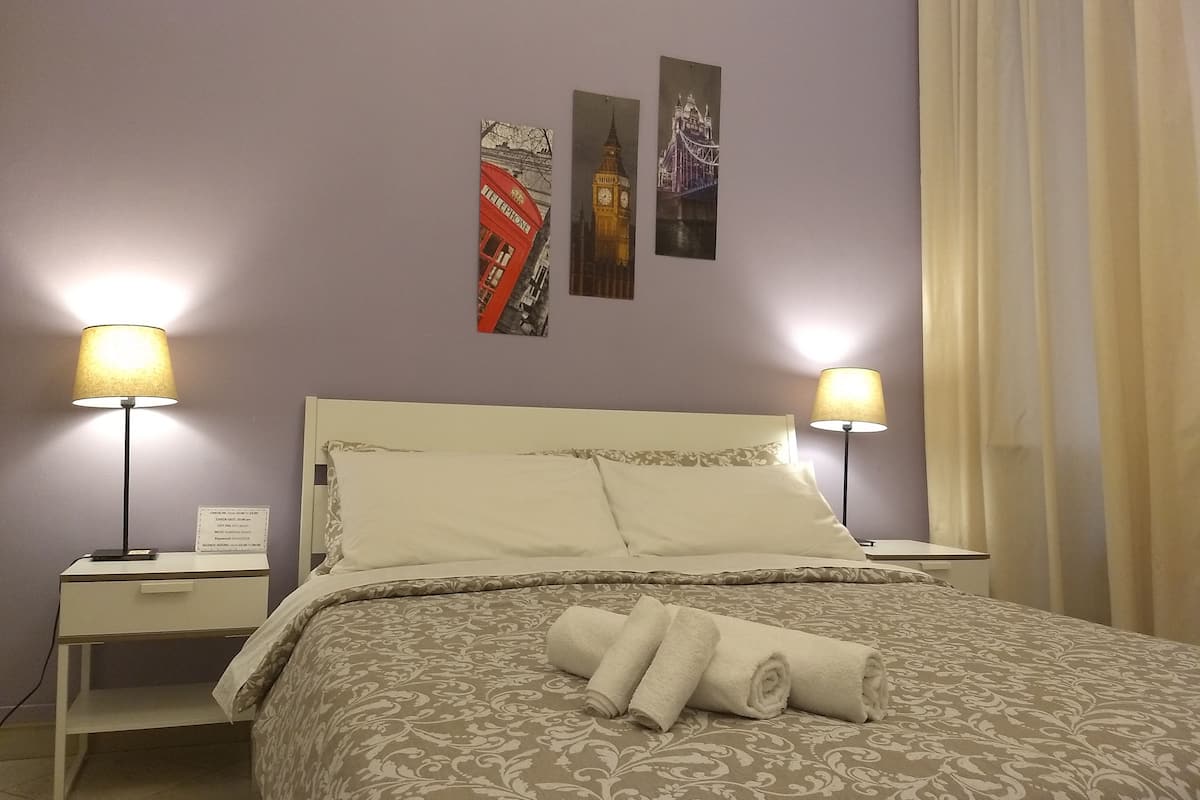A neatly made bed with a patterned bedspread, two bedside lamps, and three framed pictures on the wall.