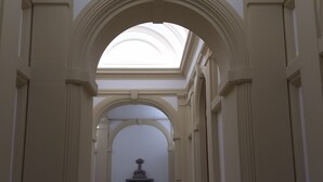 Um corredor com claraboia, teto abobadado e uma fonte central.