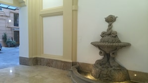 Uma fonte de pedra com esculturas detalhadas em uma área de recepção com piso de azulejos e parede simples.