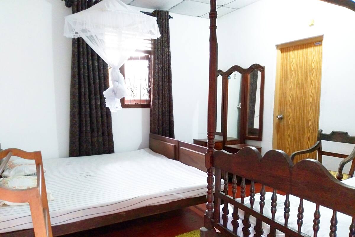 A bedroom with a four-poster bed, a wooden door, and a window with curtains.