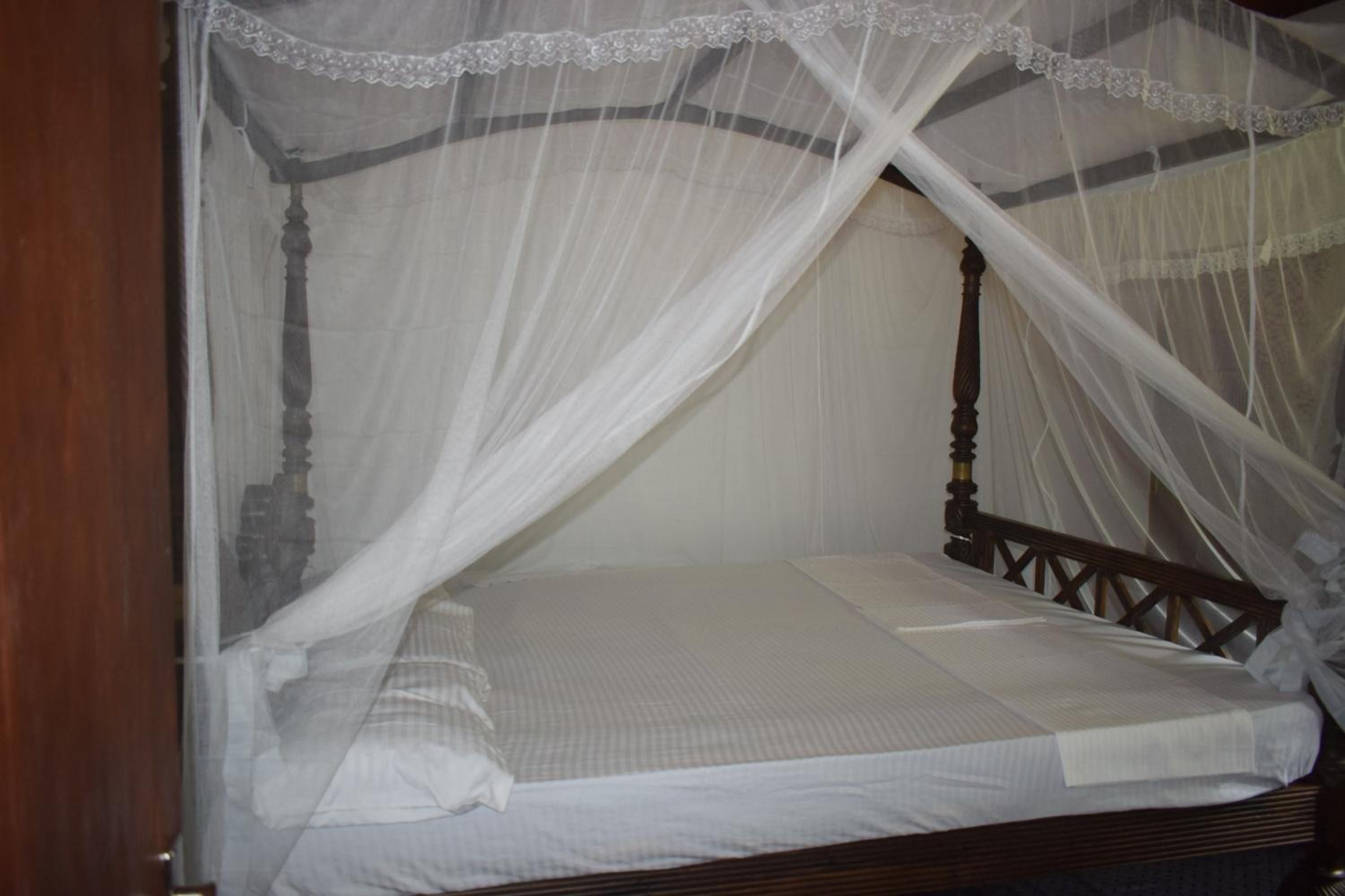 Una cama individual con estructura de madera y colchón blanco, cubierta por un dosel blanco con encaje.