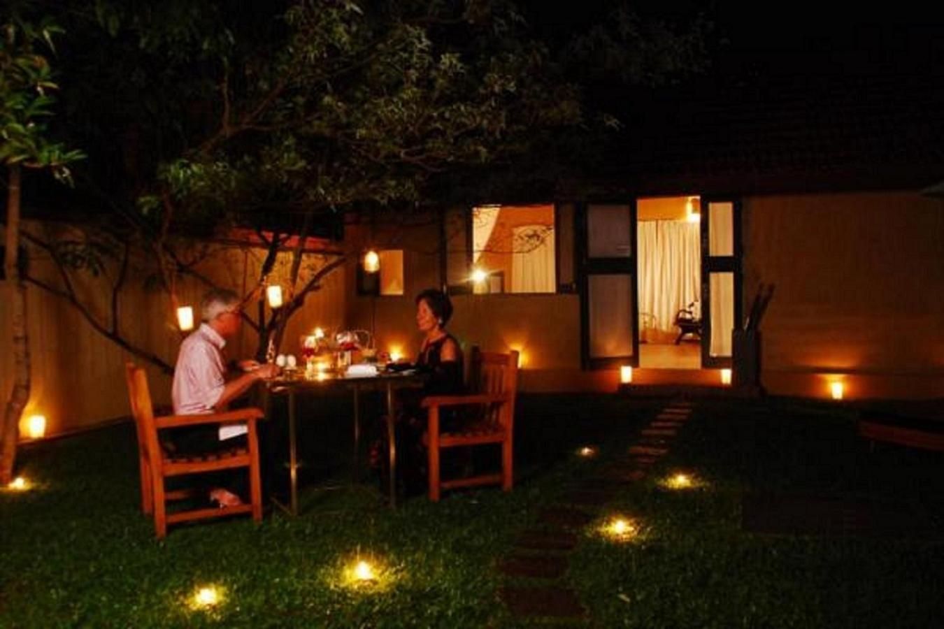 An outdoor dining area with a table and chairs, surrounded by a garden with small lights.