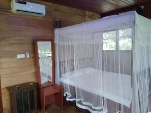 A room with a bed covered by a mosquito net, a wooden cabinet, and an air conditioning unit. - Green herbal Ayurvedic Eco-Lodge (Unawatuna)