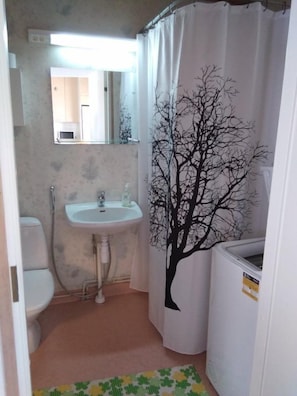 A small bathroom with a white sink, a mirror above it, a toilet, and a shower curtain with a tree design.