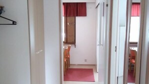 Een gang met een zwarte mat die leidt naar een kamer met een rood gordijn en een houten deur.