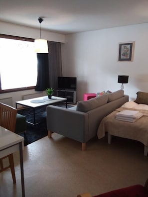 A modern living room with a sofa, a dining table, a TV, and a small plant.