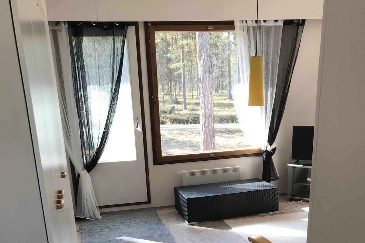 A room with a large window, a bench, a TV, and a door.
