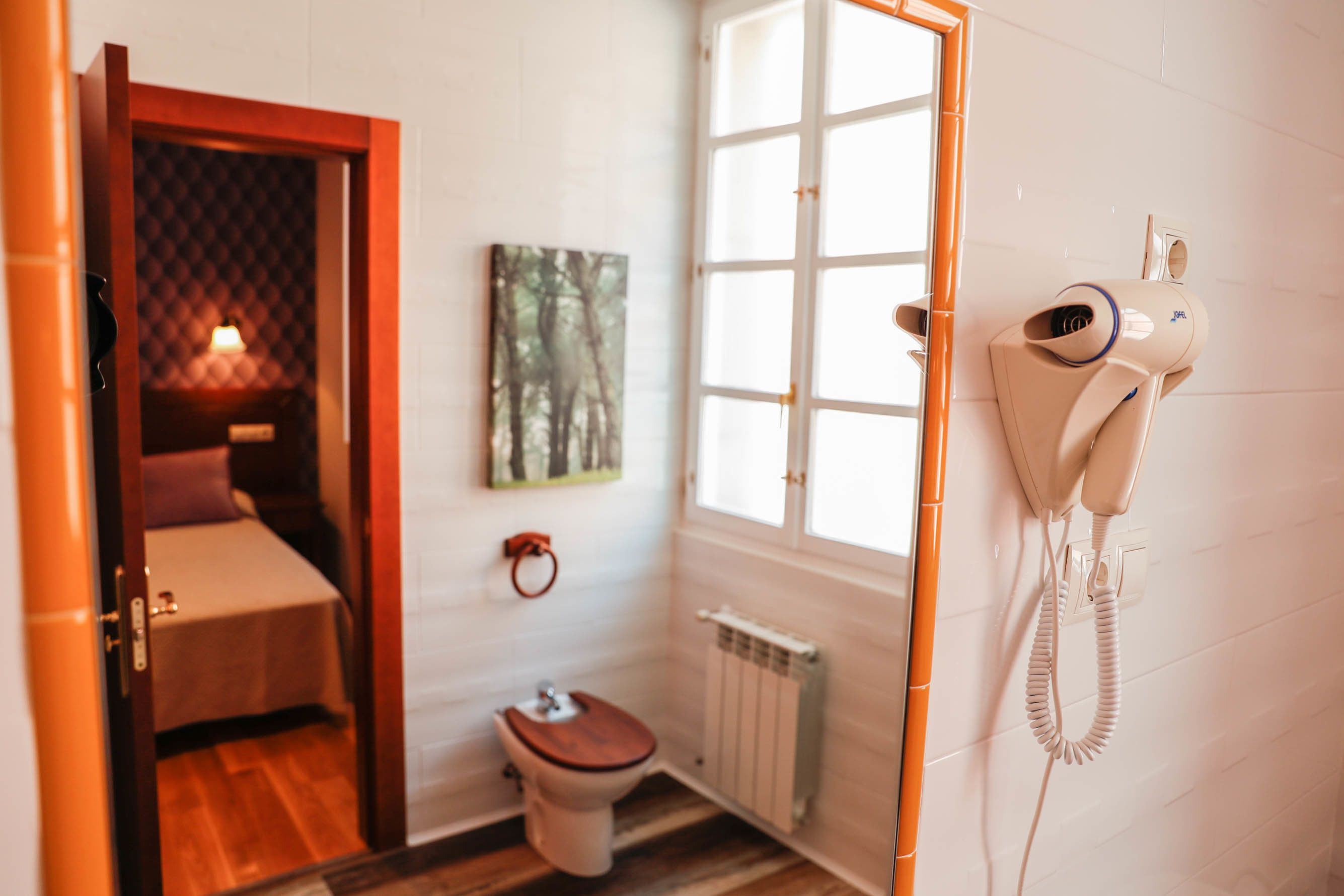 Una habitación pequeña con suelo de madera, una cama individual, un inodoro y un radiador.