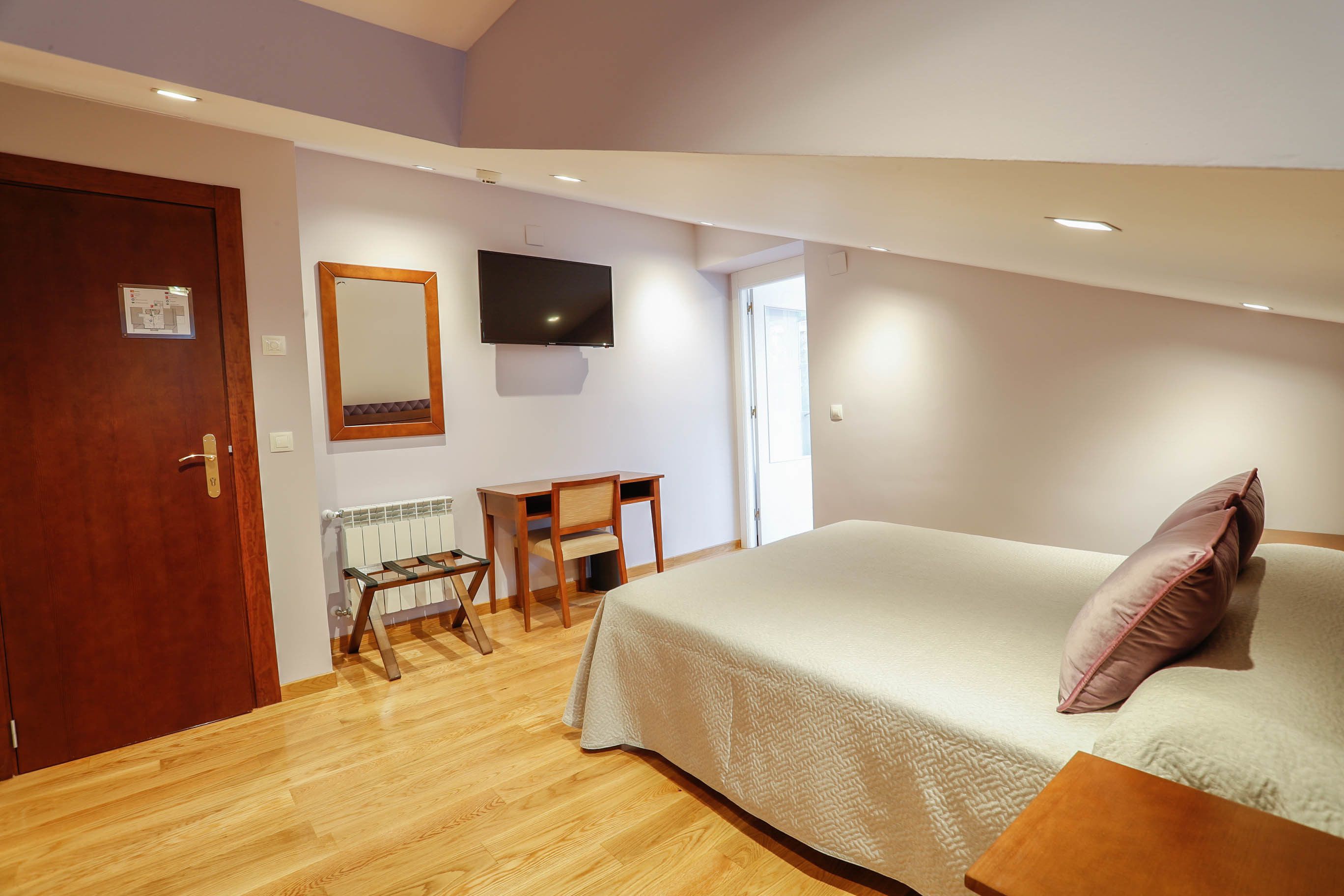 A bedroom with a bed, a desk, a chair, a television, and a door.