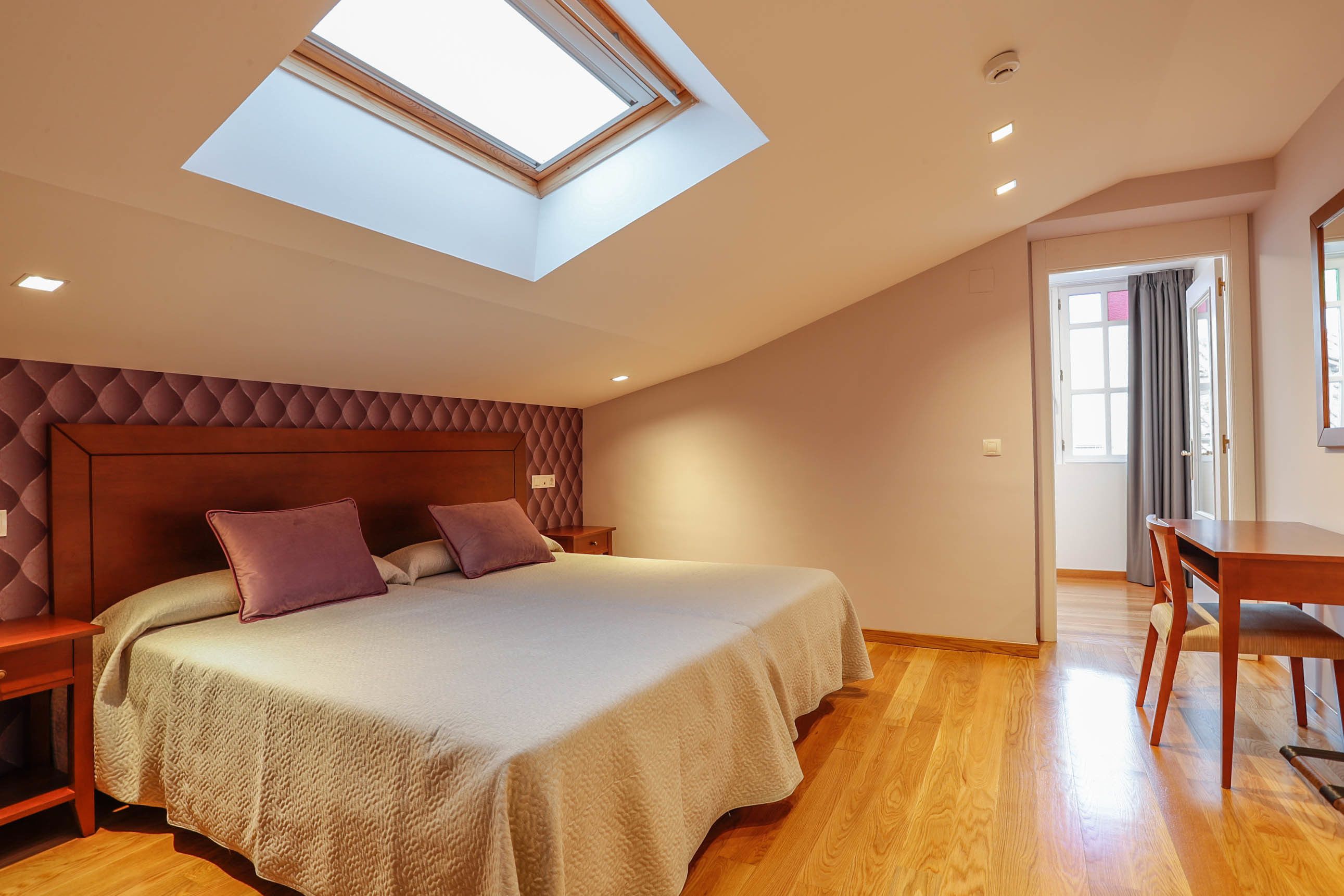 Un dormitorio con tragaluces, una cama con cabecero, un escritorio y una silla.