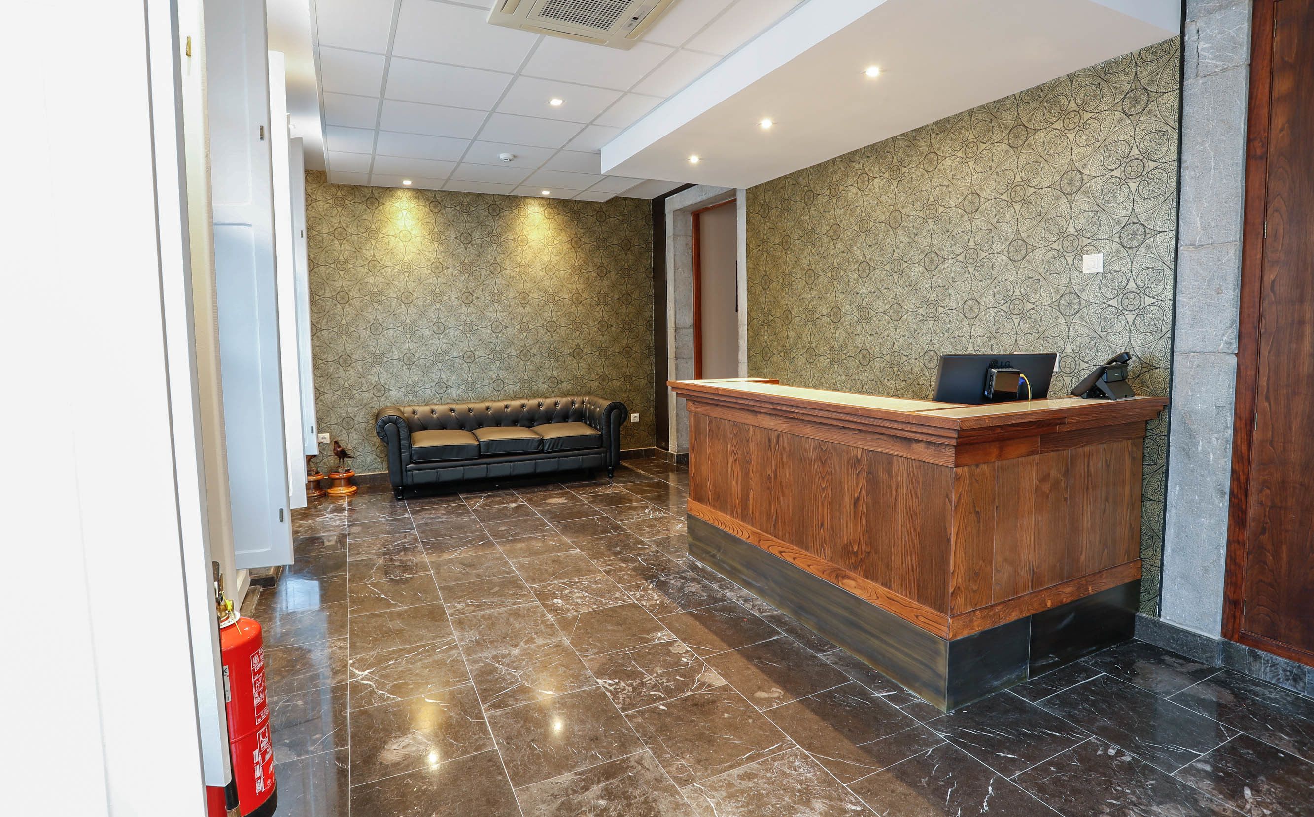 A reception area with a wooden desk, a leather sofa, patterned wallpaper, and a fire extinguisher.