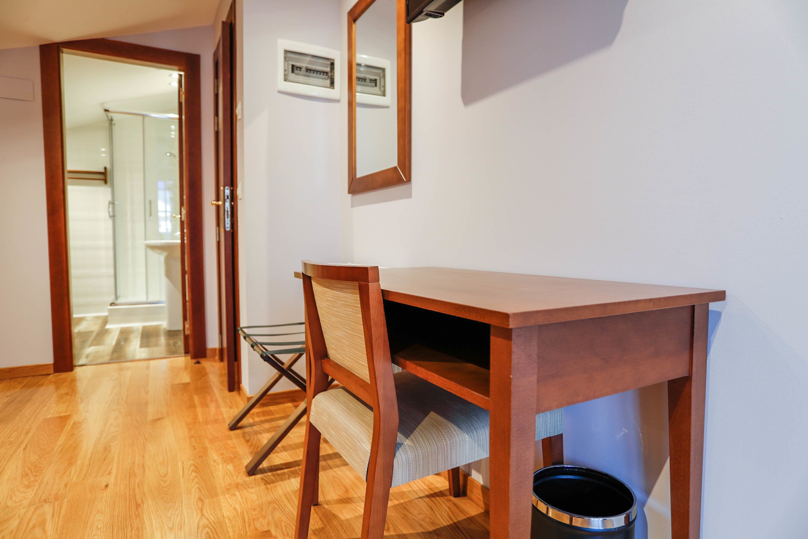 A wooden desk with a chair, a trash can, and a framed picture on the wall.