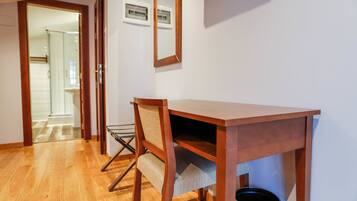 A wooden desk with a chair, a trash can, and a framed picture on the wall.