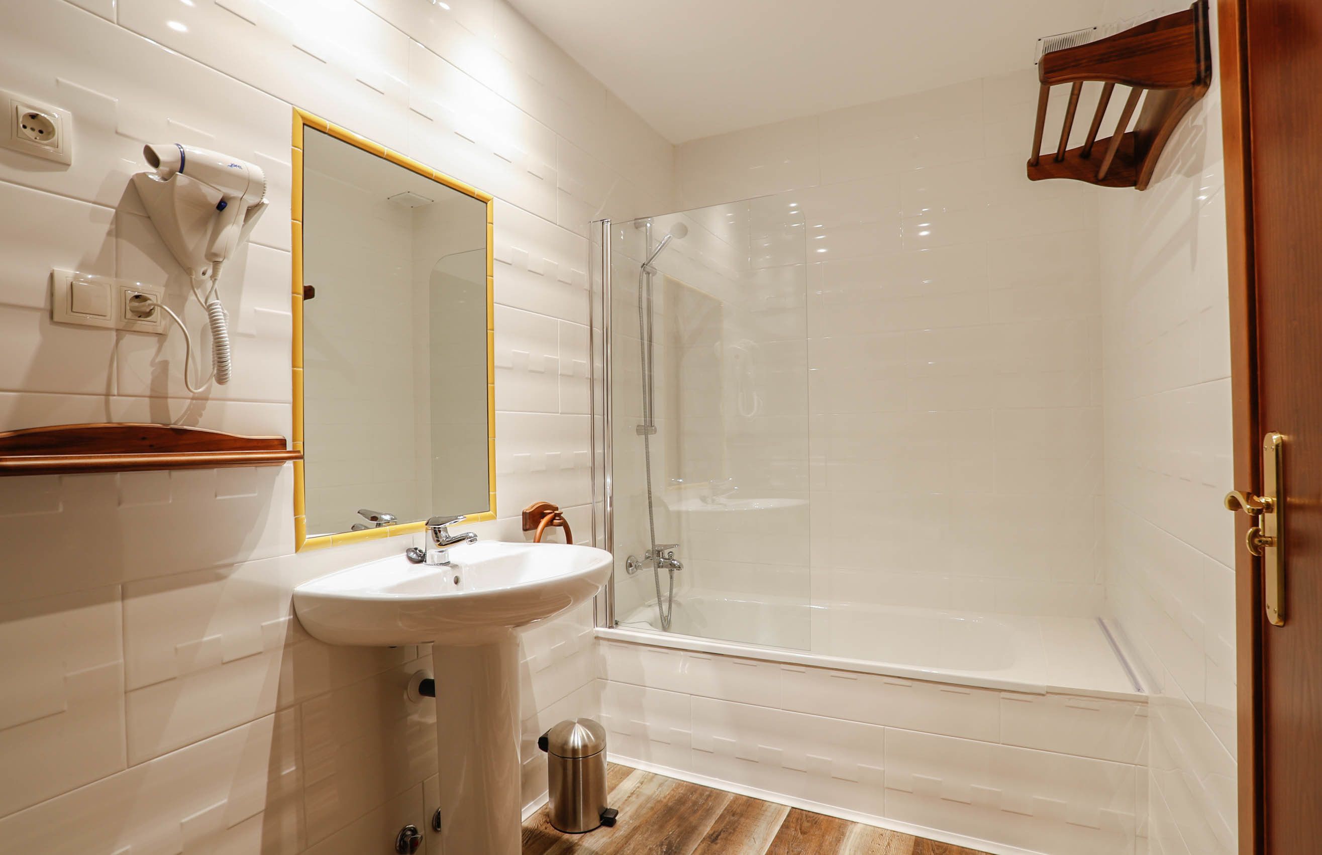 Un baño moderno con ducha de vidrio, lavamanos con espejo y un secador de pelo montado en la pared.