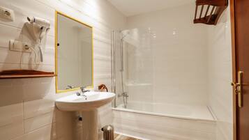 Un baño moderno con ducha de vidrio, lavamanos con espejo y un secador de pelo montado en la pared.