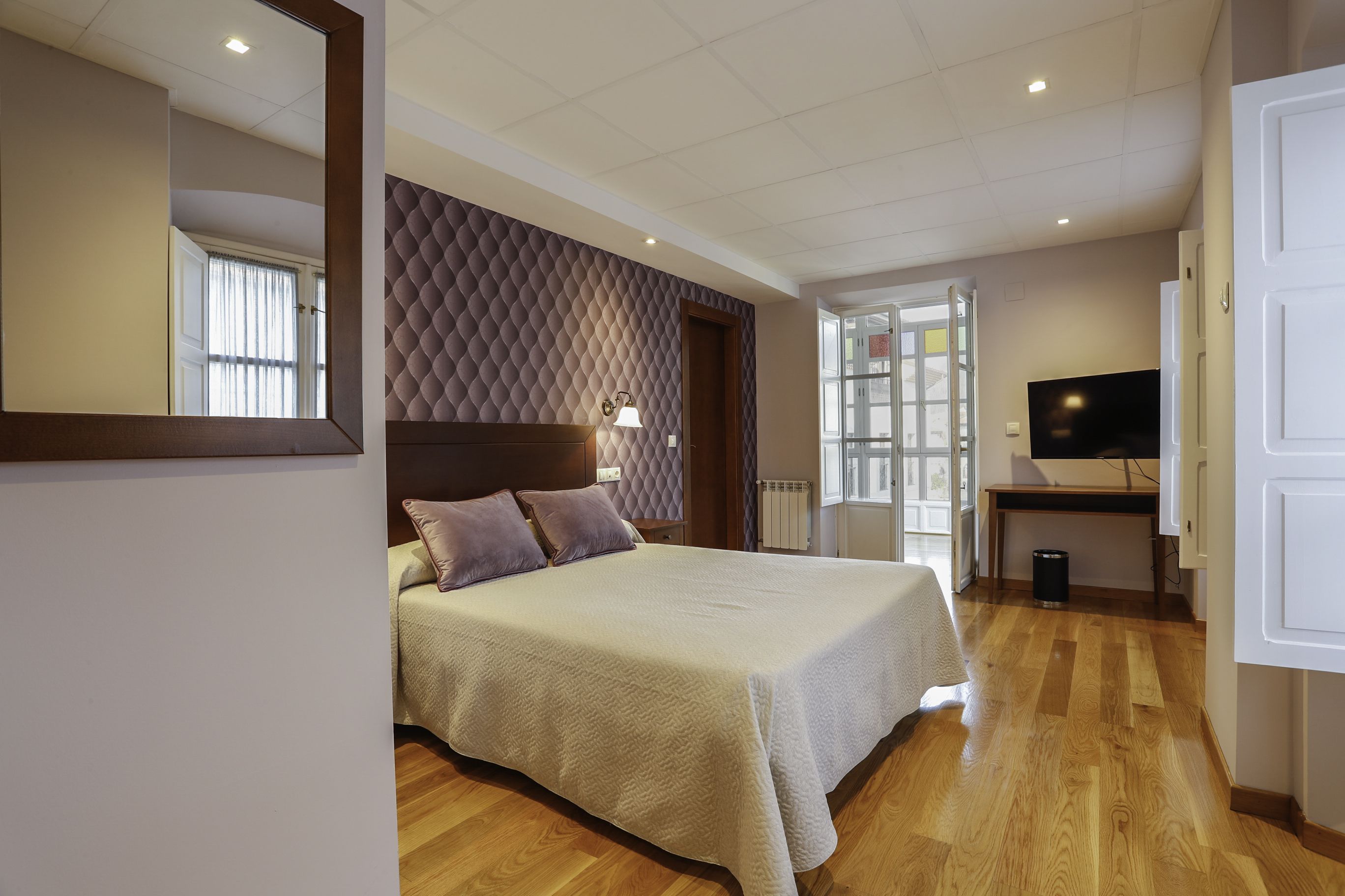 A hotel room with a large bed, a desk with a TV, and a window with curtains.