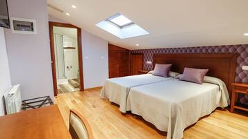 Un dormitorio con dos camas, un tragaluz, piso de madera y un baño visible a través de una puerta abierta.