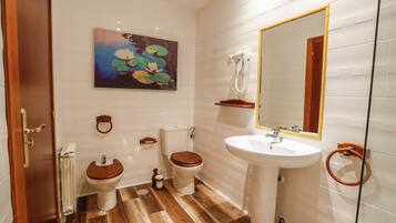 Een badkamer met een houten vloer, witte tegels, een toilet, een bidet, een wastafel en een spiegel.
