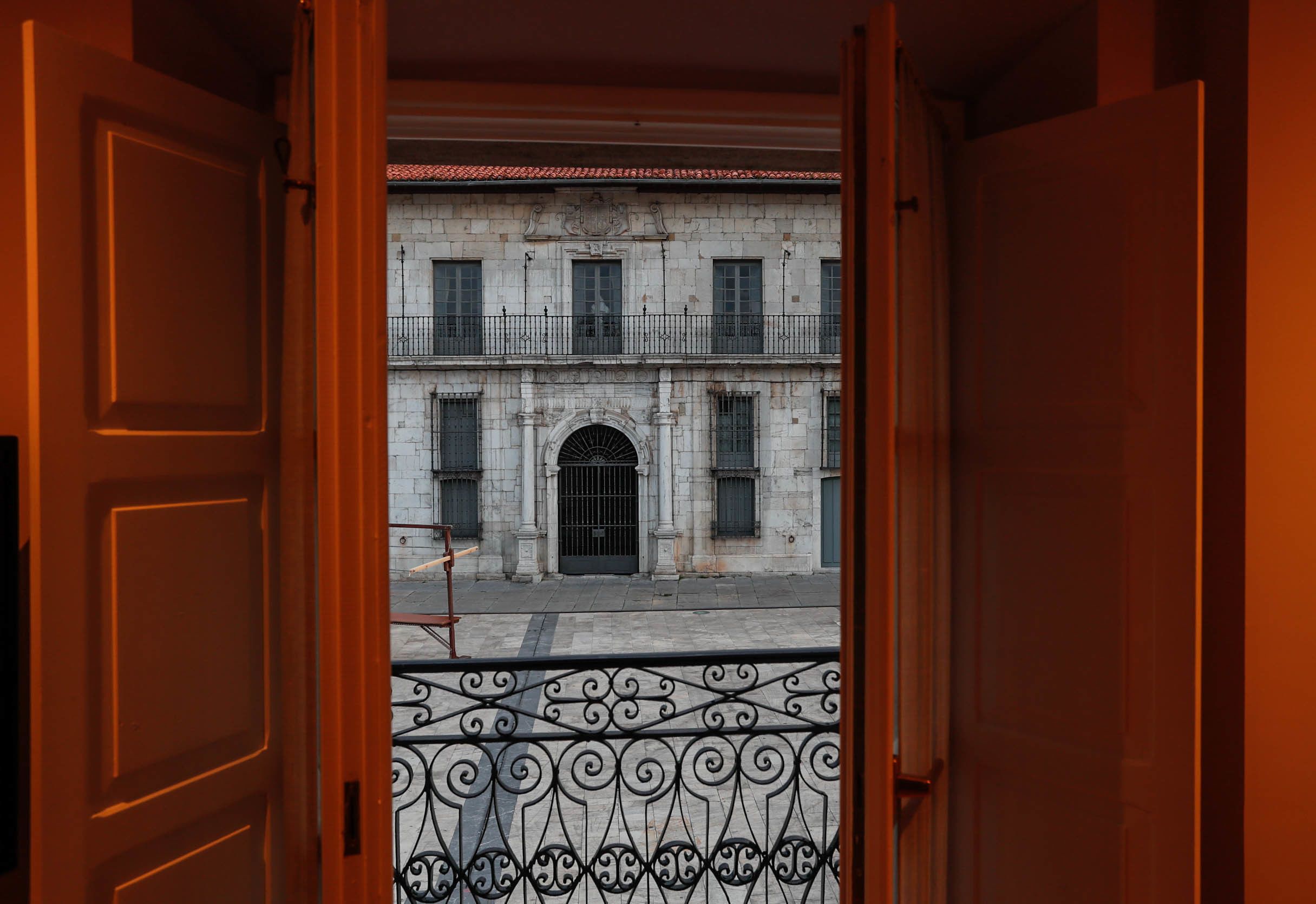 Puerta abierta que da a un patio con un edificio de piedra, una valla de hierro forjado y una reja.