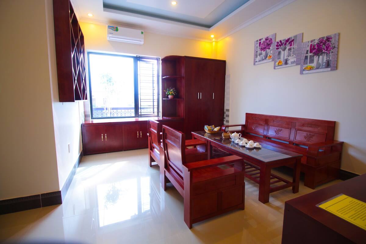 Una habitación con un sofá, una mesa y un armario. Se ve una ventana con persianas y una pared decorada con cuadros.
