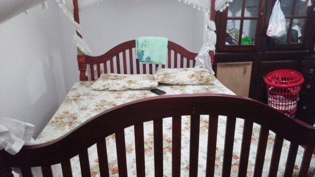 Uma cama com colcha florida, cabeceira de madeira e um dossel branco.