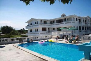 A large pool with a white building in the background. - Milien Continental (Port-au-Prince)
