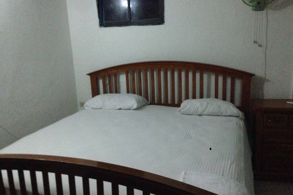 A single-bed room with a wooden headboard, white bedding, and a small bedside table with a lamp.