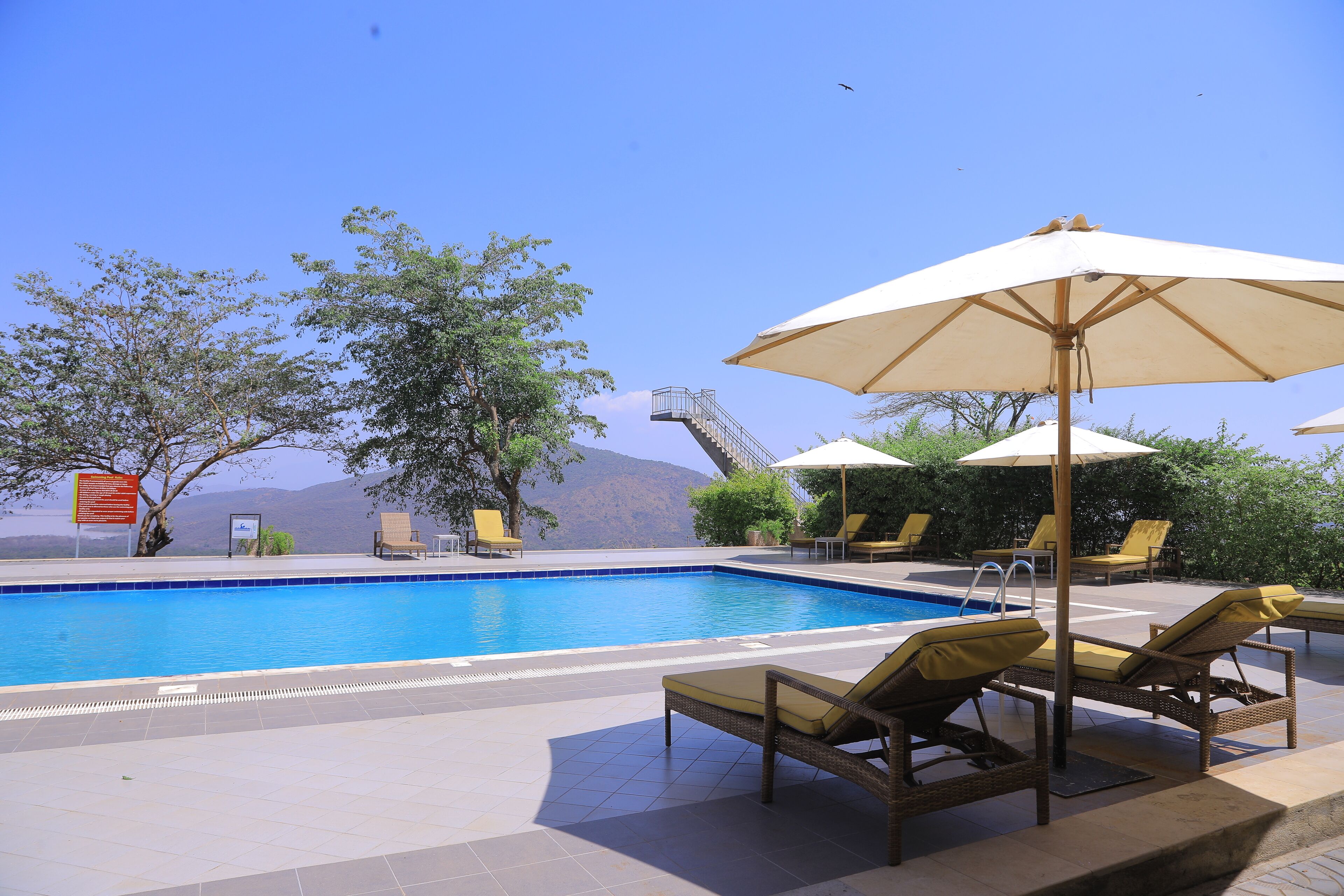 A swimming pool with lounge chairs and umbrellas, surrounded by trees and a view of mountains.