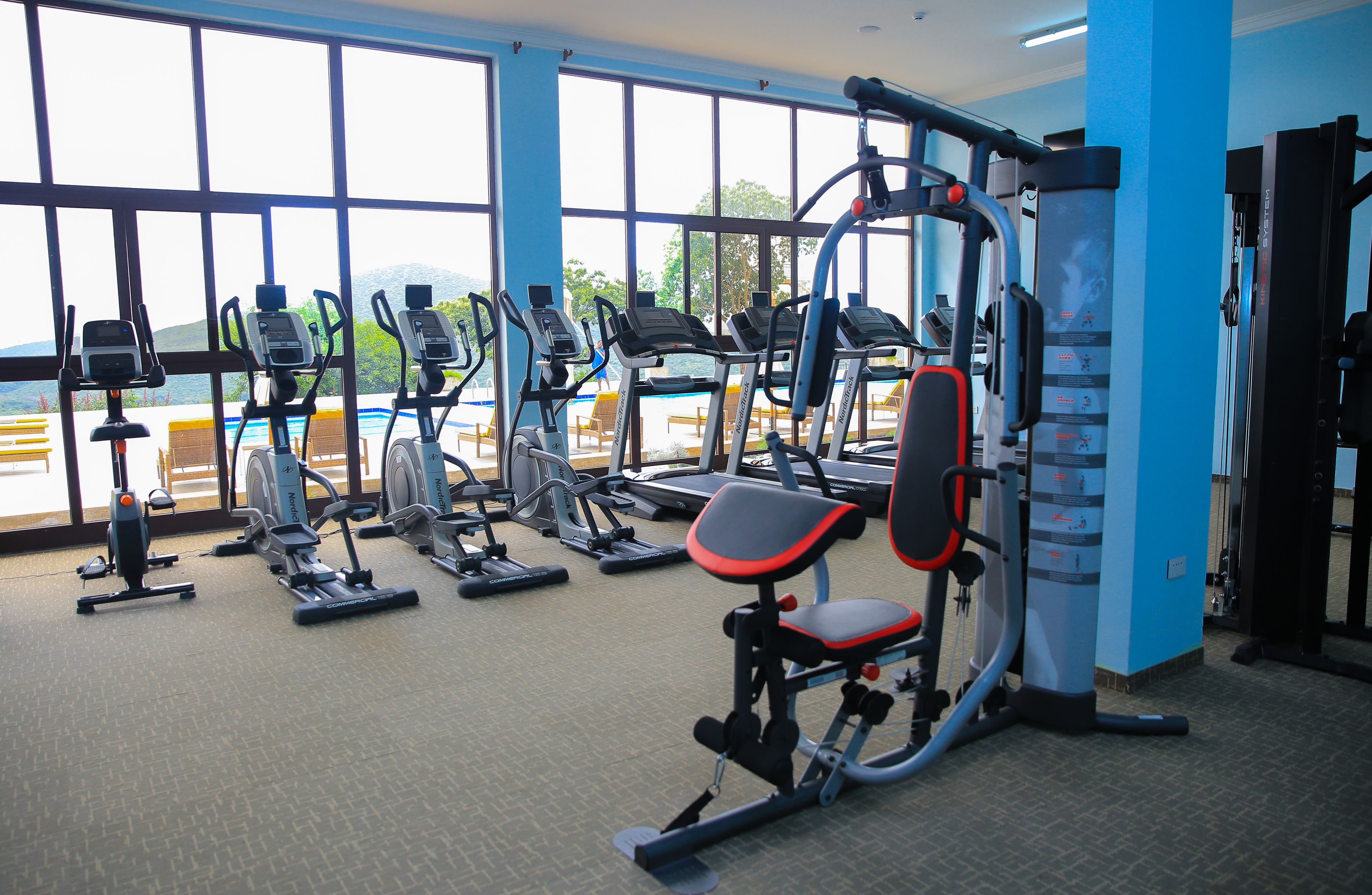 Un gimnasio con diferentes máquinas de ejercicio, ventanas amplias y vista al mar.
