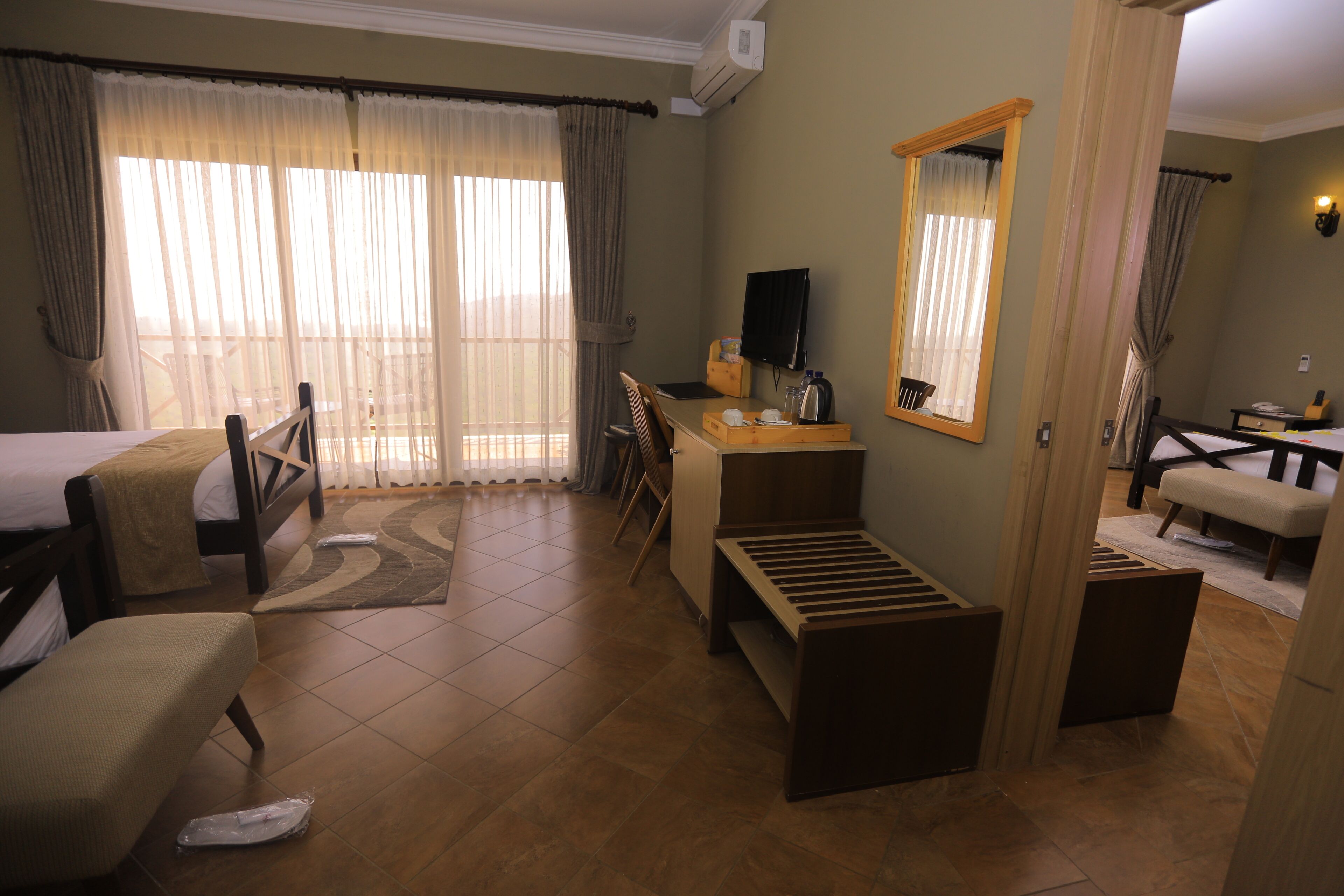 Una habitación de hotel con cama, escritorio, silla, espejo y ventana con cortinas.