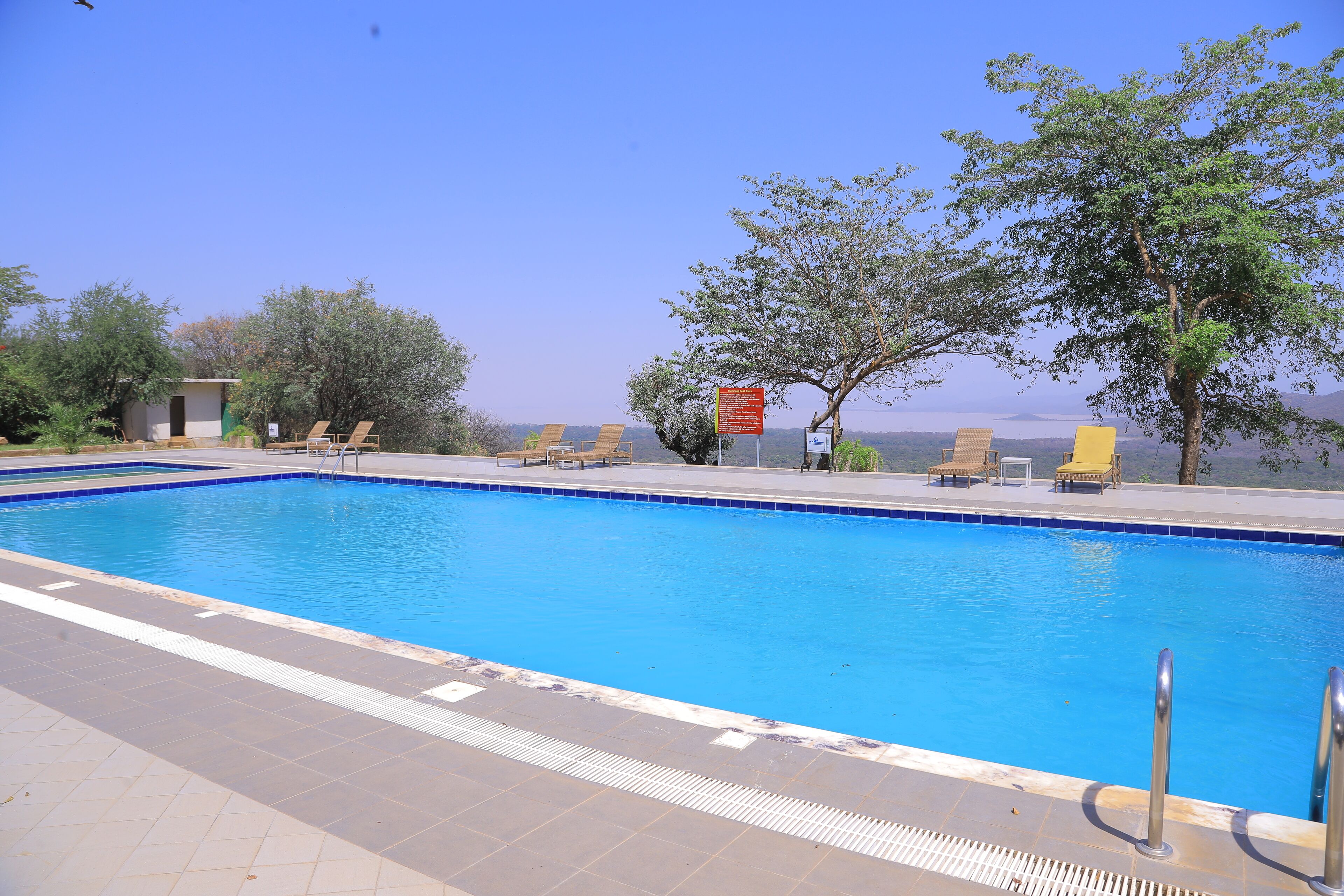 A swimming pool with clear blue water, surrounded by lounge chairs and a small building.