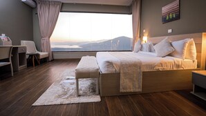 A hotel room with a large bed, a desk, a chair, a view of the mountains, and a painting on the wall. - Haile Resort Arbaminch (Arba Minch)