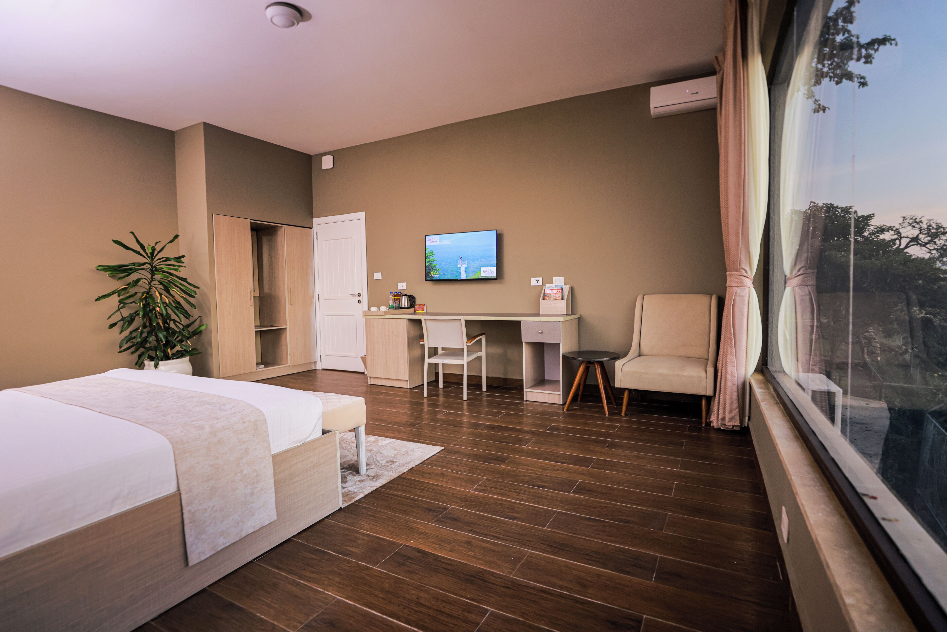 A bedroom with a bed, desk, chair, and a TV on the wall.