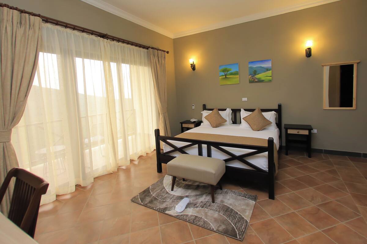 A bedroom with a bed, a nightstand, a chair, a bench, a wall-mounted lamp, and two paintings.
