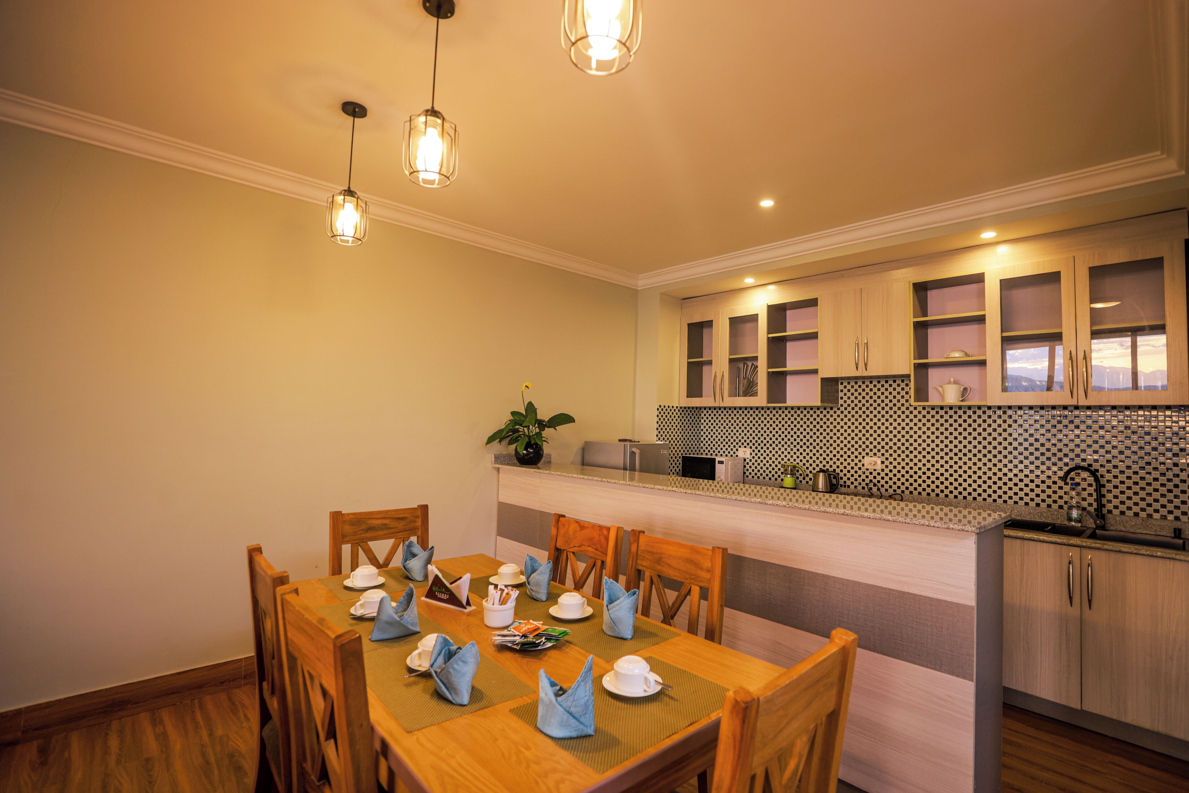 A dining area with a wooden table set for four, a kitchen with a checkered backsplash, and pendant lighting.