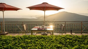 A table with a red umbrella, two chairs, and a view of a mountain range. - Haile Resort Arbaminch (Arba Minch)