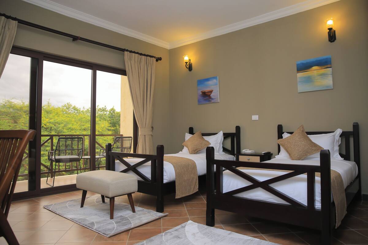 A bedroom with two beds, a balcony with chairs, and a painting on the wall.