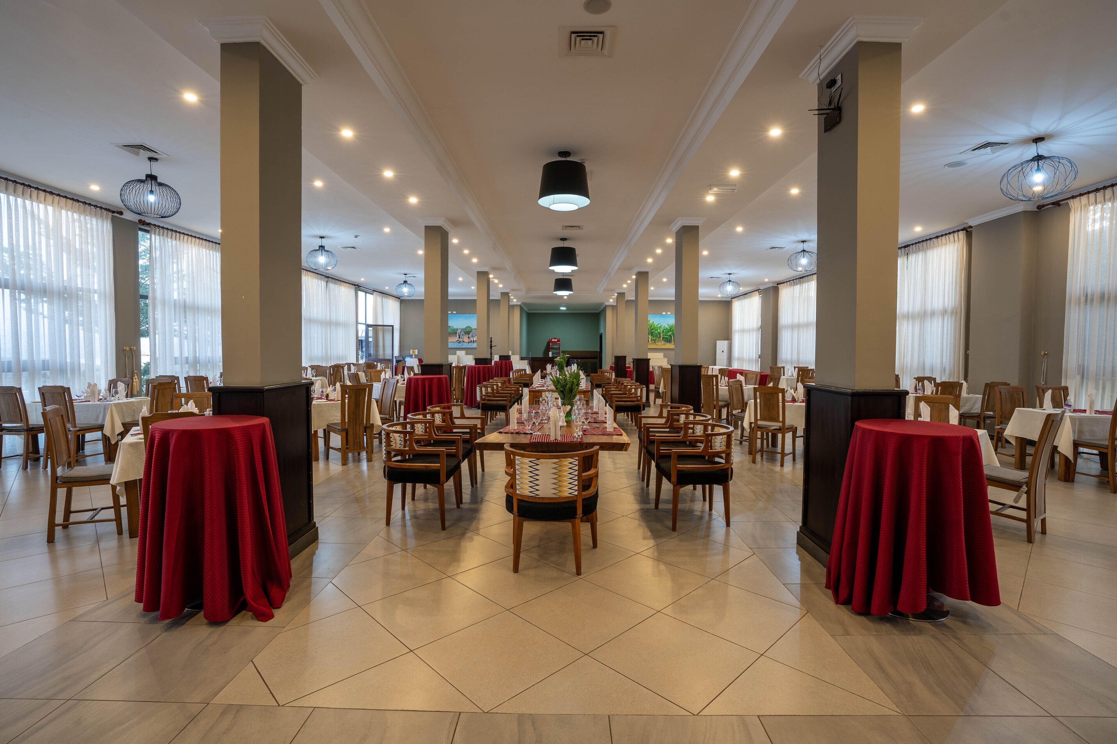 A spacious dining hall with multiple tables and chairs, large windows, and a central decorative area.