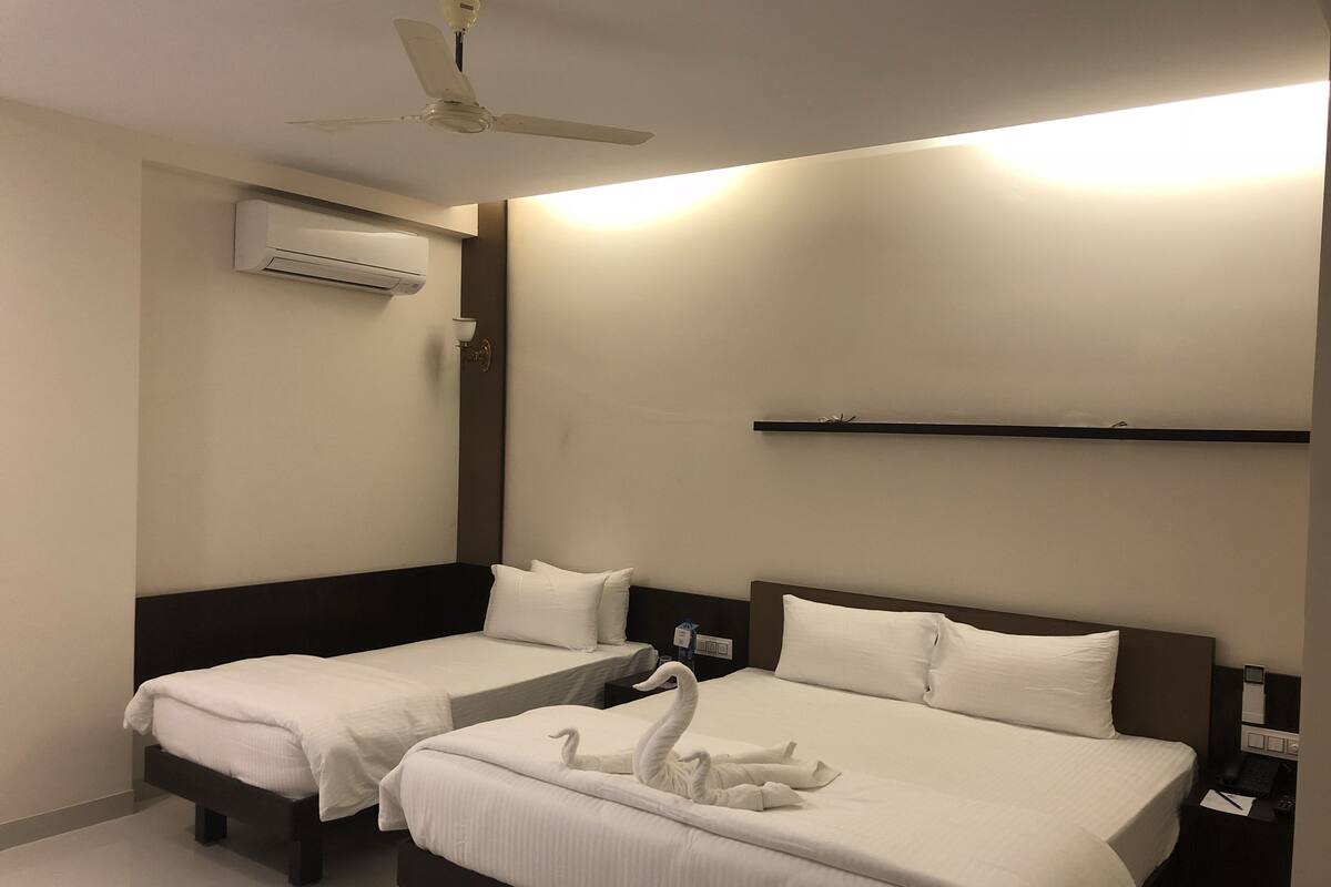 A hotel room with two beds, a ceiling fan, an air conditioning unit, a bedside table with a phone, and a wall-mounted shelf.